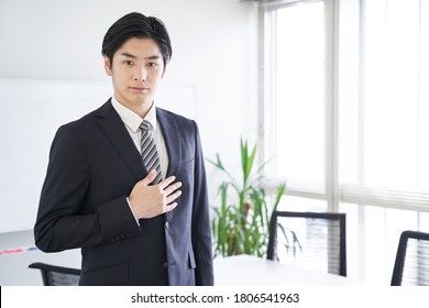 A Japanese male businessman puts his hand on his chest in a conference room - Shutterstock ID 1806541963
