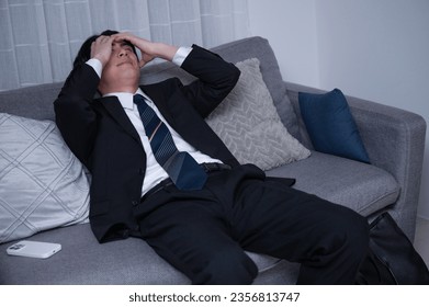 A Japanese male office worker, tired from a late-night workday, lounging on his sofa after returning home. - Powered by Shutterstock