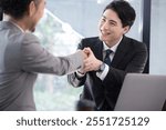 A Japanese male salesman smiles and shakes hands happily after closing a deal.