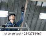 Japanese male worker in denim work clothes working at height. Checking ceilings, equipment and structure.