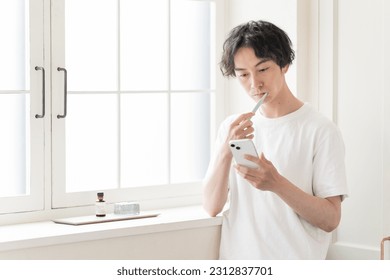 Japanese man looking at his phone while brushing his teeth.