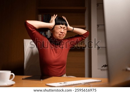 Japanese manager overwhelmed with problems sitting in front of the computer with hands on the head feeling stressed and furious.