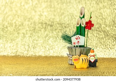 Japanese New Year's Greeting Card of a bamboo kadomatsu with the words congratulations for the welcoming spring, a kagami mochi rice cake and a cute figurine of a roaring tiger on a golden background.