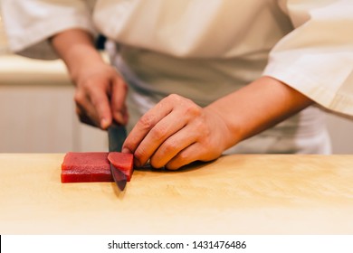 Japanese Omakase Chef cut bluefin tuna (Otoro in Japanese) neatly by knife on wooden kitchen counter for making sushi. Japanese luxury meal.