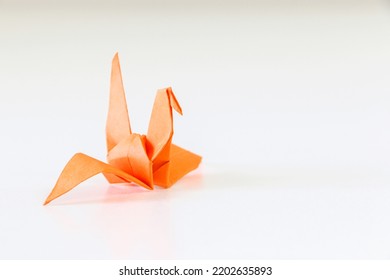 Japanese Origami Crane Folded Using Orange Paper, Isolated On Left Of White Background