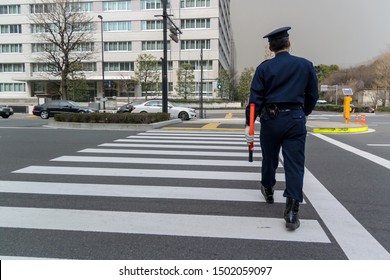 Japanese police officer is walking along a crosswalk.