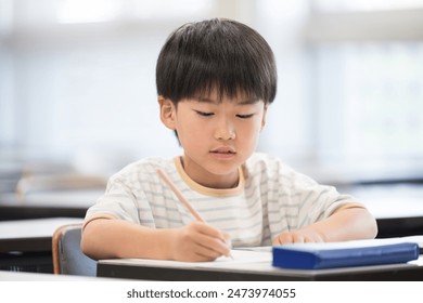 Japanese primary school boy studying and holding a pencil during class in a classroom. - Powered by Shutterstock