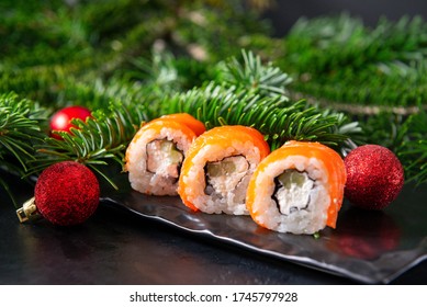 Japanese rolls with salmon, green tree branch, red Christmas balls on a black background, sushi,