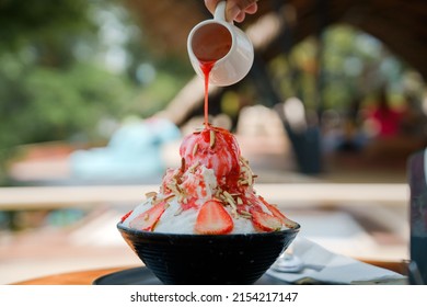 Japanese shaved ice dessert , Hand pouring sweet strawberry sauce on ice cream. Served with strawberry kakigori bingsu topped with almond stick condensed milk. Traditional summer dessert in Japan. - Shutterstock ID 2154217147