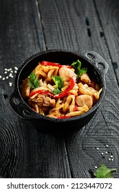 Japanese stir fryed udon noodles in wok. Udon noodle with chiken and vegetables on wooden background. Asian noodles on black table with ingredients. Wok menu