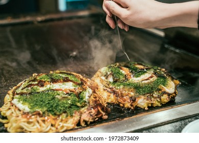 Japanese Style Pancake Okonomiyaki Handmade On Hot Grill Plate At Restaurant. Female Hands Customer Ready To Eat Okonomiyaki On Teppanyaki Pan. Local Food In Osaka Japan.