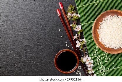 Japanese sushi chopsticks, soy sauce bowl, rice and sakura blossom on black stone background. Top view with copy space  - Powered by Shutterstock