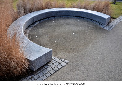 Japanese tall dry grasses for the winter tied in sheaves. in the arch of the flowerbed surround the granite bench in the park. The bench is bent like a horseshoe, with a smooth surface by the sidewalk - Powered by Shutterstock