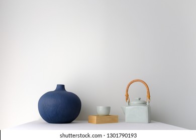 Japanese White Ceramic Teapot With Wooden Handle And Tea Cup And A Blue Oriental Ceramic Vase On White Table Top On White Background In Natural Light With Copy Space. Minimal Asian Interior Styling.