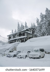 Japanese winter scenery with Cars on parking covered with snow, traditional countryside house and pine forest in background