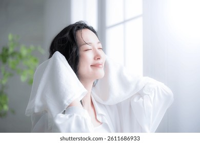 Mujer japonesa secándose el pelo mojado por la mañana o después de tomar un baño por una ventana retroiluminada. Imagen de secado de toallas. Primer plano desde la perspectiva de la cámara. Mirando hacia arriba y cerrando los ojos.