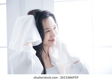 Mujer japonesa secándose el pelo mojado por la mañana o después de un baño por una ventana retroiluminada. Imagen de secado de toallas. Primer plano de una cara sonriente.