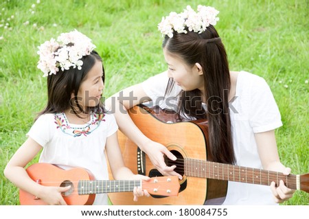 Japanese woman and girl playing guitar in the grass