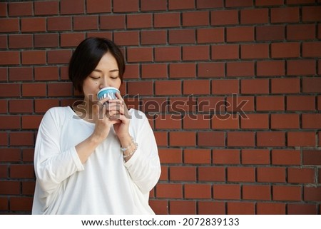 Japanese woman holding coffee in front of a brick