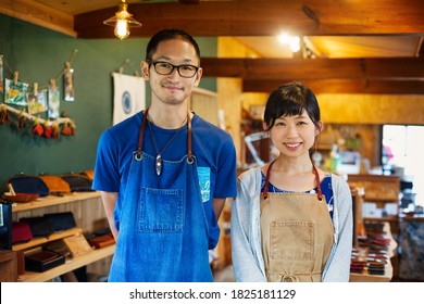 Japanese woman and man wearing blue apron standing in a leather shop, smiling at camera. - Shutterstock ID 1825181129