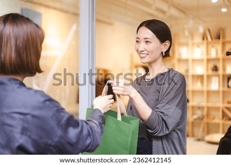 A Japanese woman works at a clothing store.A store clerk puts the products purchased by a customer in a shopping bag and hands them over.