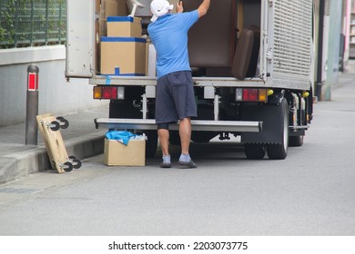 Japanese Worker Unloading Furniture From Van Outdoors. Moving Service