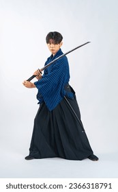 Japanese young samurai wielding katana sword in studio with white background.