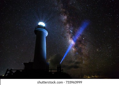 Japan's Uganzaki Lighthouse at night on the island of Ishigaki, Okinawa, with the Milky Way and a bright blue laser light aimed through it.