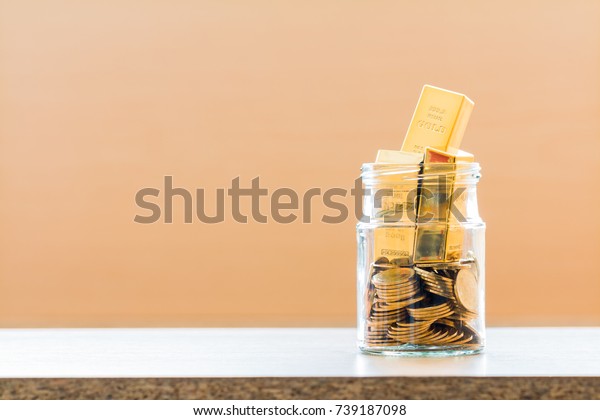 Jar bank with coin and a gold bar inside\
put on desk in the office background, Loan or a saving money for\
business investment in the future\
concept.
