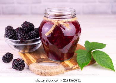 A jar of blackberry jam on a white wooden background.
