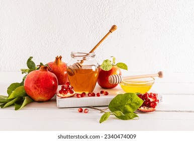 A jar and a bowl of delicious honey, ripe pomegranates and apples for the celebration of the Roshashan holiday. white background. front view. - Shutterstock ID 2340474009