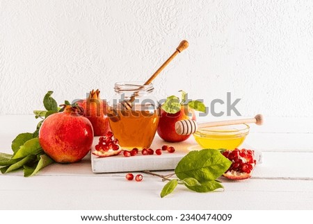 A jar and a bowl of delicious honey, ripe pomegranates and apples for the celebration of the Roshashan holiday. white background. front view.