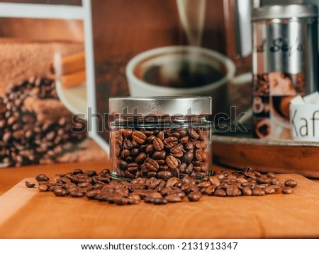 Jar of brown coffee beans on a wooden kitchen shelf  Detailed coffee in the foreground  Other coffee accessories in the background 