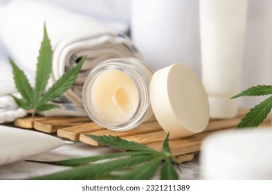 Jar with CBD lip balm and green cannabis leaves near bottles and towel in bathroom close up on a wooden tray. Organic skincare product. Alternative cosmetics
 - Powered by Shutterstock