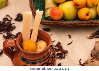 Jar of Christmas fruit punch with cane, tejocote and guava. Basket with fruits, apple. On the table tamarind and hibiscus leaves