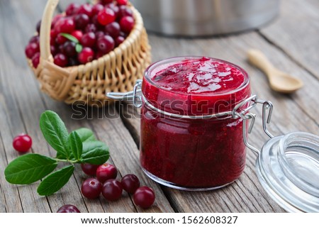 Jar of crushed cranberries for sauce or jam and basket of bog berries on background. 