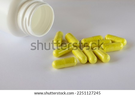 A jar of food supplements lies next to sprinkled yellow quercetin capsules on a white background.