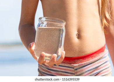 Jar With Fresh River Water In A Child's Hand On The Beach