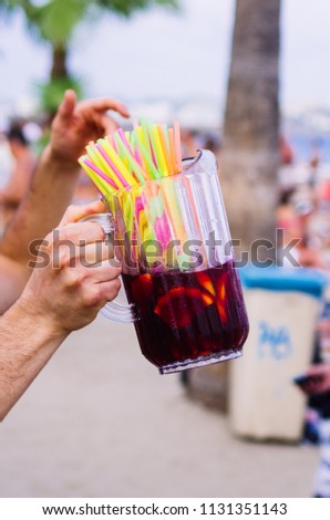 jar full of sangria and colored straws, unknow person, beach.