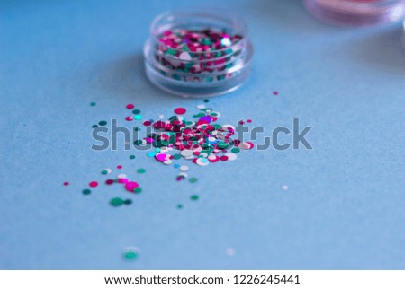 Jar of glitter for nail design, scattered on a blue background.