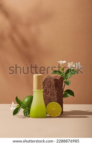 A jar with gradient color displayed with Lime slice, a stone and white flowers on brown background. Lime (Citrus aurantiifolia) can remove the stratum corneum and dead skin cells