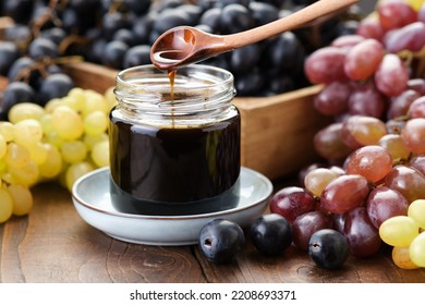 Jar of grape molasses, grape syrup. Sweetener, cough medicine. Black, green and purple grapes on kitchen table.