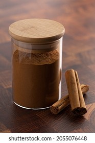 Jar Of Ground Cinnamon And Cinnamon Sticks On Wooden Butcher Block