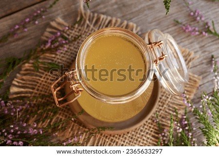 A jar of herbal syrup with fresh heather flowers harvested in the forest