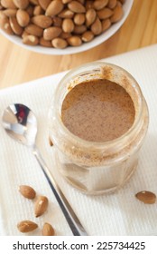 A Jar Of Homemade Almond Butter With A Bowl Of Fresh Almonds At An Angled View From Above