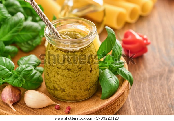 Jar with homemade pesto sauce on rustic\
background with parmesan cheese, olive oil, sause pesto, basil and\
garlic. Copy space\
background.