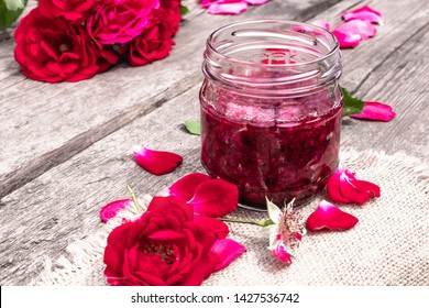 Jar of jam of rose petals on a wooden table with flowers of roses. Flower confiture. Healthy food. Copy space