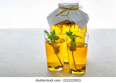 A Jar Of Kombucha And Two Glass Cups Of Kombucha Are Decorated With Mint On A Light Gray Concrete Table. Low Alcohol Fermented Carbonated Drink