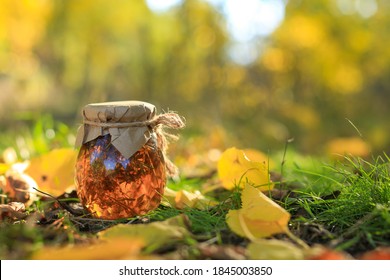 A jar with linden honey and sprigs of thyme wrapped in linen cloth against the background of an autumn landscape with yellow leaves.