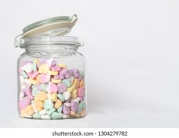 Jar of pastel candy hearts against white background with negative space on right for text or graphic.
